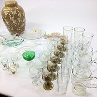 Overview of assorted glasses, decorative plates, and large beige ceramic vase with white floral pattern