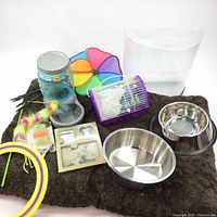 Photo showing pet supplies including brown dog bed, small purple and white hamster cage, assorted pet toys, water bottle, picture frame, and stainless steel bowls.