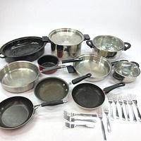 Full view of pots, pans, and cutlery laid out on a white surface.