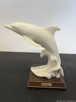 Front angle view of the white dolphin statue showing the dynamic leaping pose and wooden base.