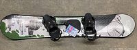 Top view of the Echos snowboard showing the graphic design and attached black bindings with straps.