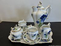 Five-piece porcelain tea set displayed on matching tray with blue rose floral pattern and gold trim