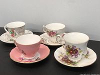 Full shot showing four tea cups with various floral patterns and matching saucers on black table