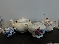 Four tea pots grouped together showing various floral designs and shapes.