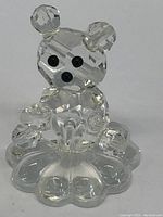 Front view of clear Swarovski crystal bear figurine sitting on flower shaped base showing faceted details and black eyes and nose.