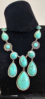 Front view of turquoise custom necklace displayed on black bust, showing teardrop and round turquoise stones with silver-tone metal settings.