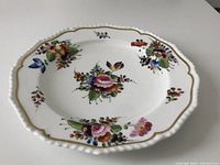 Front view of the porcelain plate showing floral decorations and scalloped edges with gold accents