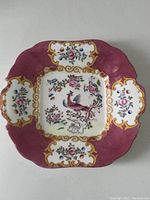 Full view of the square serving dish showing the overall detailed design with bird and floral motifs, textured purple background, and gold trim.