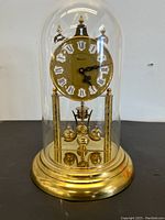 Full front view of vintage gold-tone anniversary clock with glass dome covering dial and pendulum, showing overall design and condition.