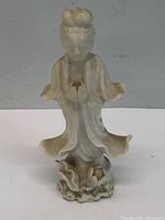 Side view of vintage Asian ceramic statue showing flowing robes and detailed base with flower.