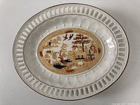 Full view of the oval Wedgwood plate showing pierced rim and central scenic pattern in warm tones.