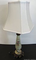 Full view of the table lamp with white fabric shade and hand painted floral lamp body over ornate metal base.