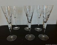 Six tall crystal champagne glasses with etched geometric patterns arranged on a black surface.