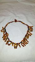 Amber and turquoise beaded choker necklace laid out on white fabric, showing textured clusters of beads and amber clasp.