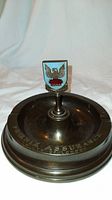 Front view of bronze ashtray showing pedestal and enamel crest.