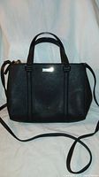 Full front view of black leather handbag showing its structured shape, two top handles, and long shoulder strap laid out.