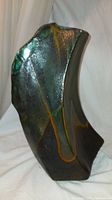 Front angled view showing the curved shape and green, black, orange glaze pattern resembling a natural stone water wave.