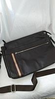 Full view of brown Danier leather messenger bag showing front zippered pocket with two-tone fabric stripes and attached adjustable brown shoulder strap.