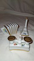 Photo showing three miniature porcelain dollhouse items: an accordion, a double inkwell, and a candlestick holder with floral and gold details.