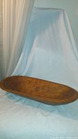 Long oval wooden bowl displayed on a white cloth background, showing the overall shape and size of the bowl.