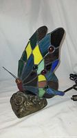 Front side view showing colorful stained glass butterfly wings and ornate floral base with power cord visible.