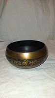 Front angled view of the singing bowl showing the engraved Tibetan script on the outer side and bronze-black metal finish.