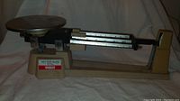 Full side view of Ohaus triple beam balance scale showing round weighing pan and labeled base.