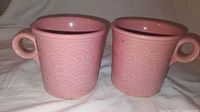 Pair of pink Fiesta Ware mugs with Art Deco embossed pattern shown side by side.