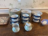 All items laid out on a wooden surface showing cups, saucers, plates, sugar and creamer, and decorative tiles