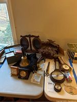 Wide view of lot on table including clocks, barometers, bell, scissors, frame and accessories