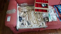 White wire basket containing assorted costume jewelry including necklaces, rings, bracelets, earrings and a red compartment jewelry box