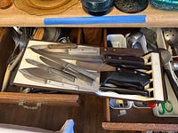 Knives with wooden and plastic handles arranged on a wooden magnetic knife block inside a drawer.