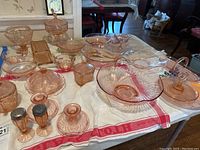 Overall view of the collection of pink depression glass pieces on table showing variety of bowls, dishes, covered candy dishes, and other glass items.