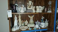 Wide view of shelf displaying various porcelain figurines, decorative bowls, and other small collectible items ranging from 2 to 8 inches tall including angels, children, and animals.