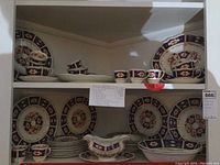 Full view of display cabinet with all china items including plates, bowls, cups, saucers, gravy boat and platters arranged on shelves showing decorative floral pattern on white china with blue and gold trim.