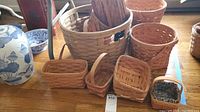 Photo displaying multiple Longaberger baskets of different sizes and shapes arranged on wooden floor.