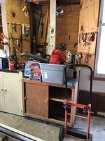 Wide view showing leaf blower, air station, chainsaw, booster cables in plastic bin on wood cabinet in garage workspace