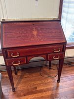Full view of the antique wooden secretary desk with floral inlay on drop front, brass edging on top and brass drawer pulls on three drawers below the slant