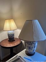 Two blue and white ceramic table lamps with pleated beige lampshades on separate wooden tables.
