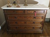 Front view of vintage wooden dresser with white stone top, showing four drawers with wooden knobs and keys in the lock.