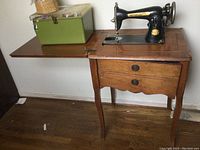 Full view of the sewing machine mounted in the wooden cabinet with the green plastic sewing box and basket on top.