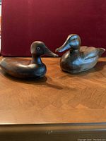 Front perspective view of two carved wood duck decoys on wood tabletop with red background, showing size and finish details.