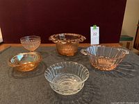 Full view of all five pieces in lot: clear bowl, amber dish, pink flower holder, pink dessert dish with knobs, and pink bowl with handles.