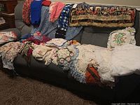 Photo of the full lot laid across sofa, showing a variety of crocheted doilies, embroidered pieces, scarves and the Lord's Supper tapestry.