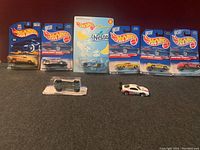 Eight Hot Wheels Nestle branded diecast cars shown together. Six cars remain sealed in original packaging while two are loose. Packaging shows Nestle candy branding and Hot Wheels logo. Loose cars include Sweetarts and one other themed design.