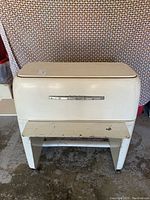 Front view of vintage Kenmore mangle/iron, cream color, heavy metal body with legs and top closed.
