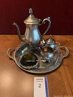 Silver plate tea and coffee set including coffee pot, creamer, sugar bowl, jelly or butter server with small spoon, displayed on the serving tray. Shows tarnishing and used condition.