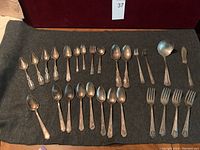Full lot of silver plated flatware pieces laid out on felt background showcasing various spoons, forks, ladle, and butter knife.