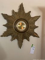 Full view of vintage starburst molded wall clock with peeling paint hanging on wall.
