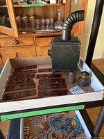 The antique black metal photo slide projector with flexible exhaust pipe, eyepiece, and lamp, set inside a cardboard box with slides arranged around it.